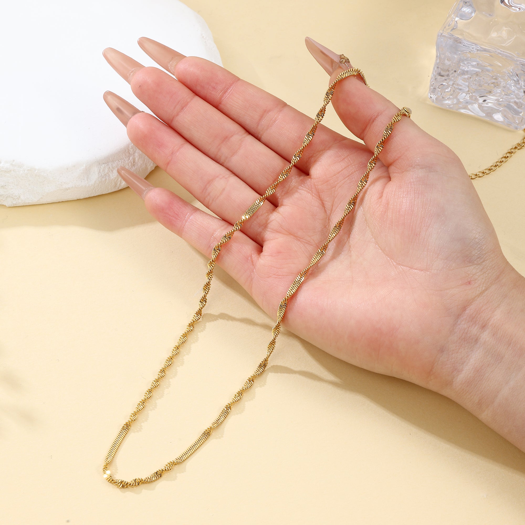 Gold chain held by a hand on a beige background